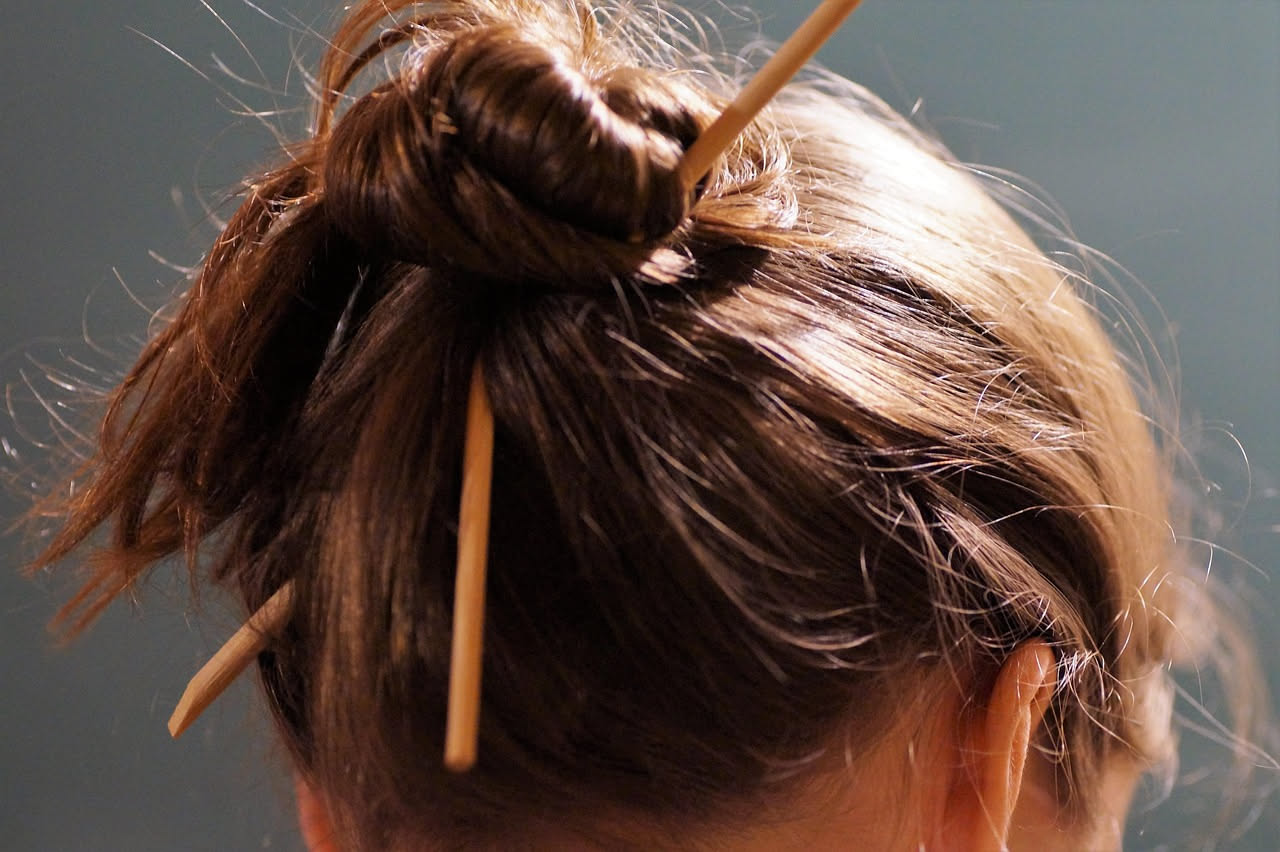 Busto di marmo di donna romana con capelli raccolti in uno chignon alto, decorato con perle e nastri d'oro, espressione serena e maestosa