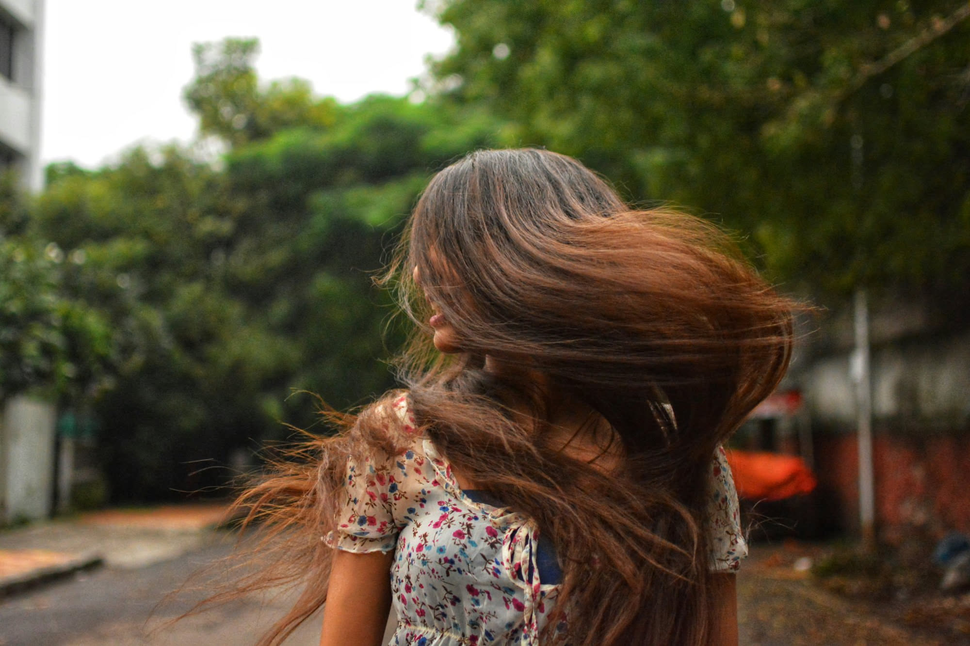 Flacone di olio per capelli versato su capelli lunghi e ondulati, con dettagli di idratazione e lucentezza naturale